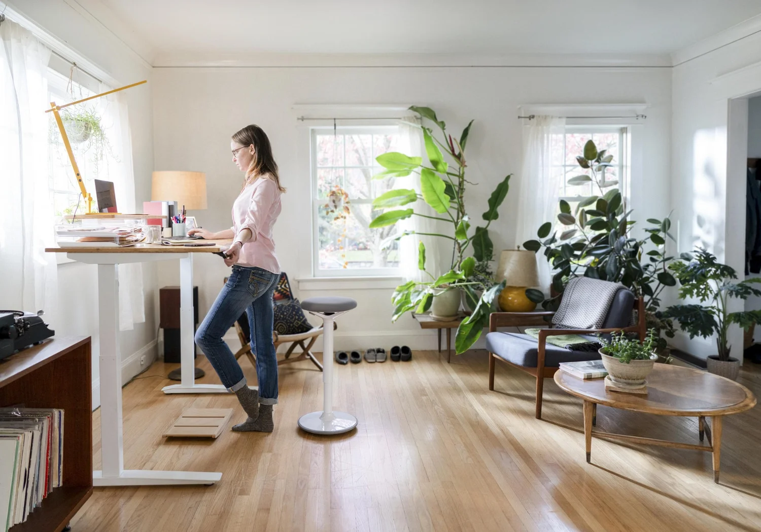 Woman using a standing desk in a bright plant-filled workspace