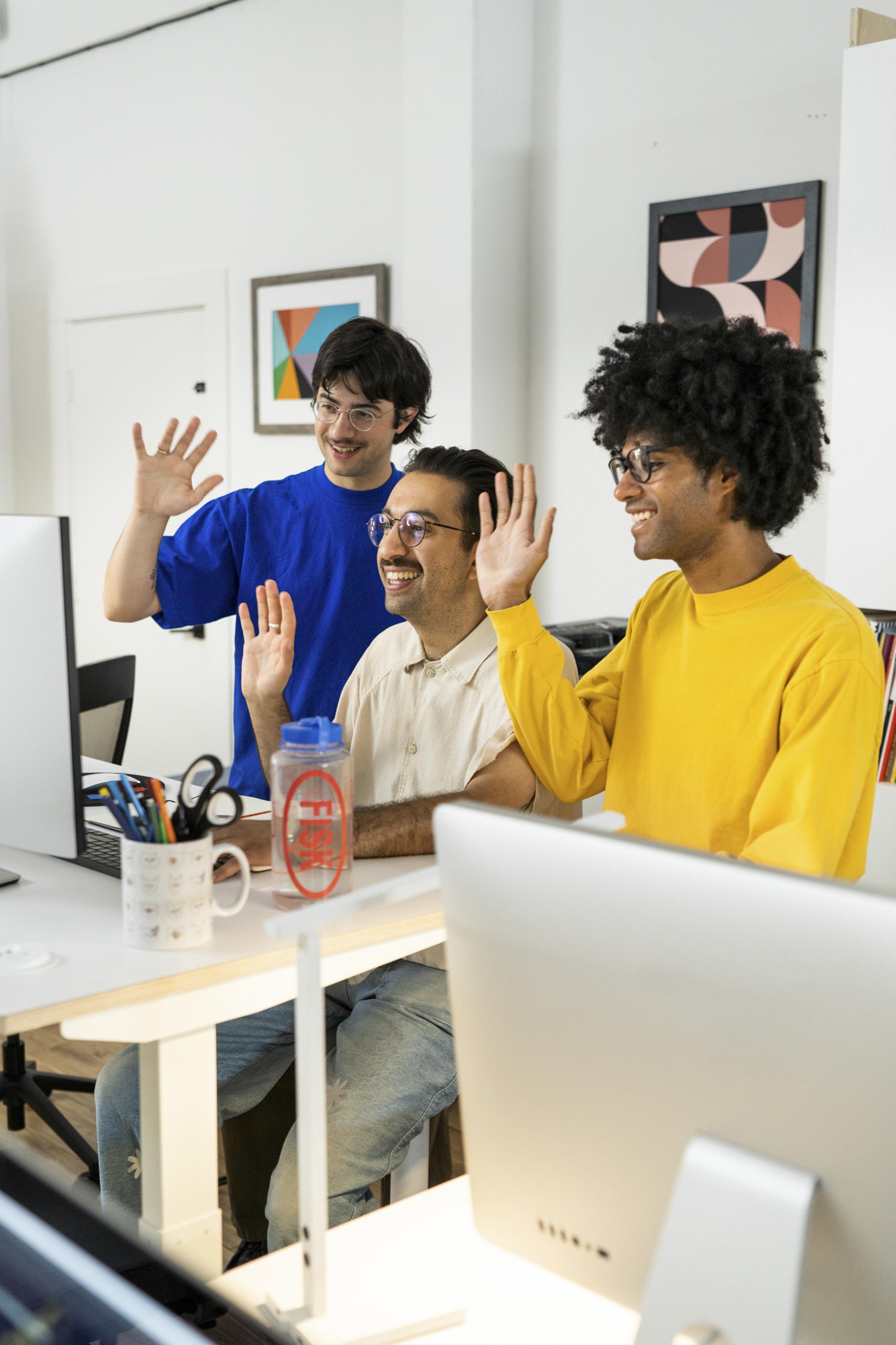 Three creative colleagues greeting one another in a bright studio