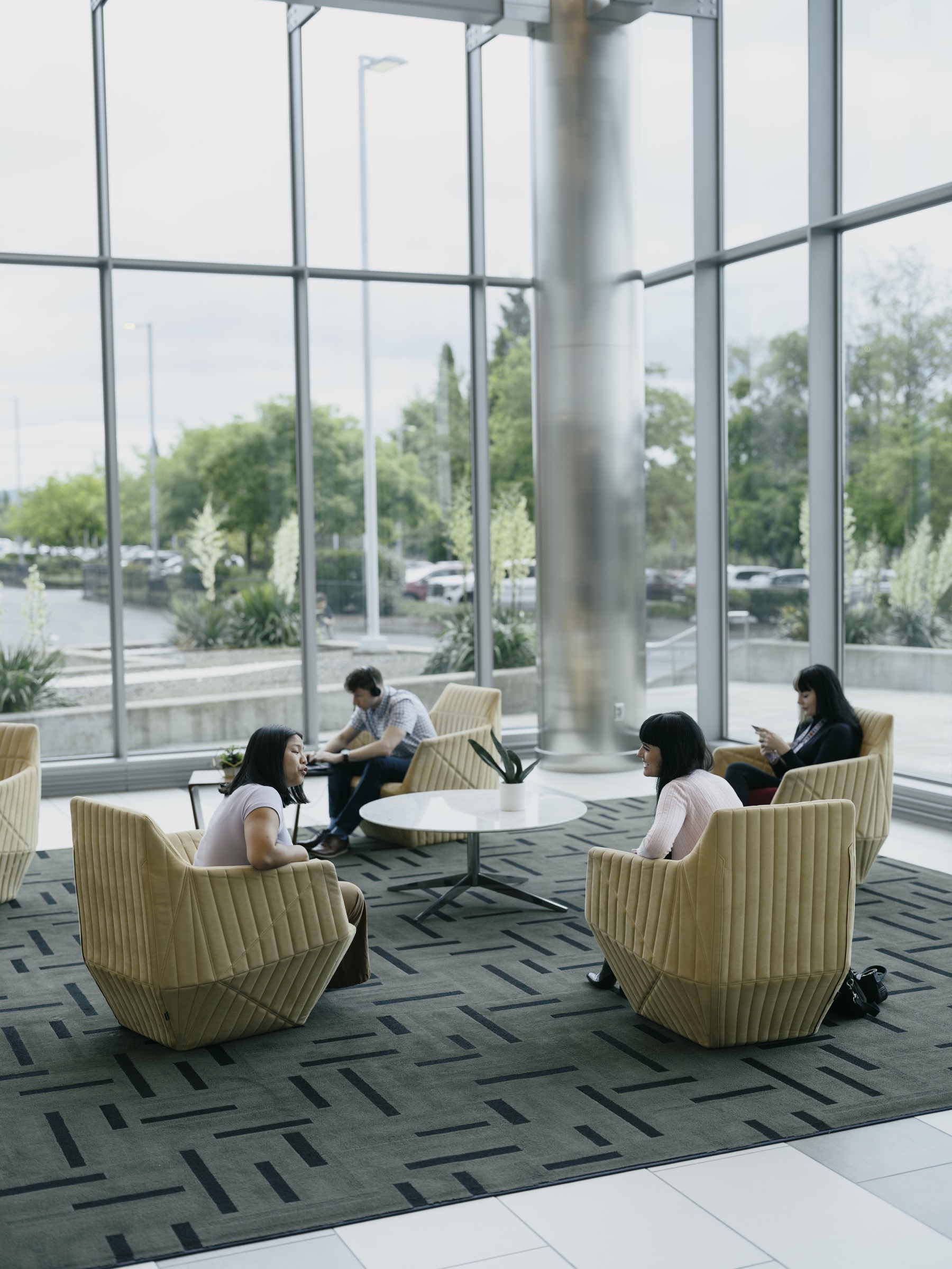 People meeting in lounge chairs beside tall glass windows