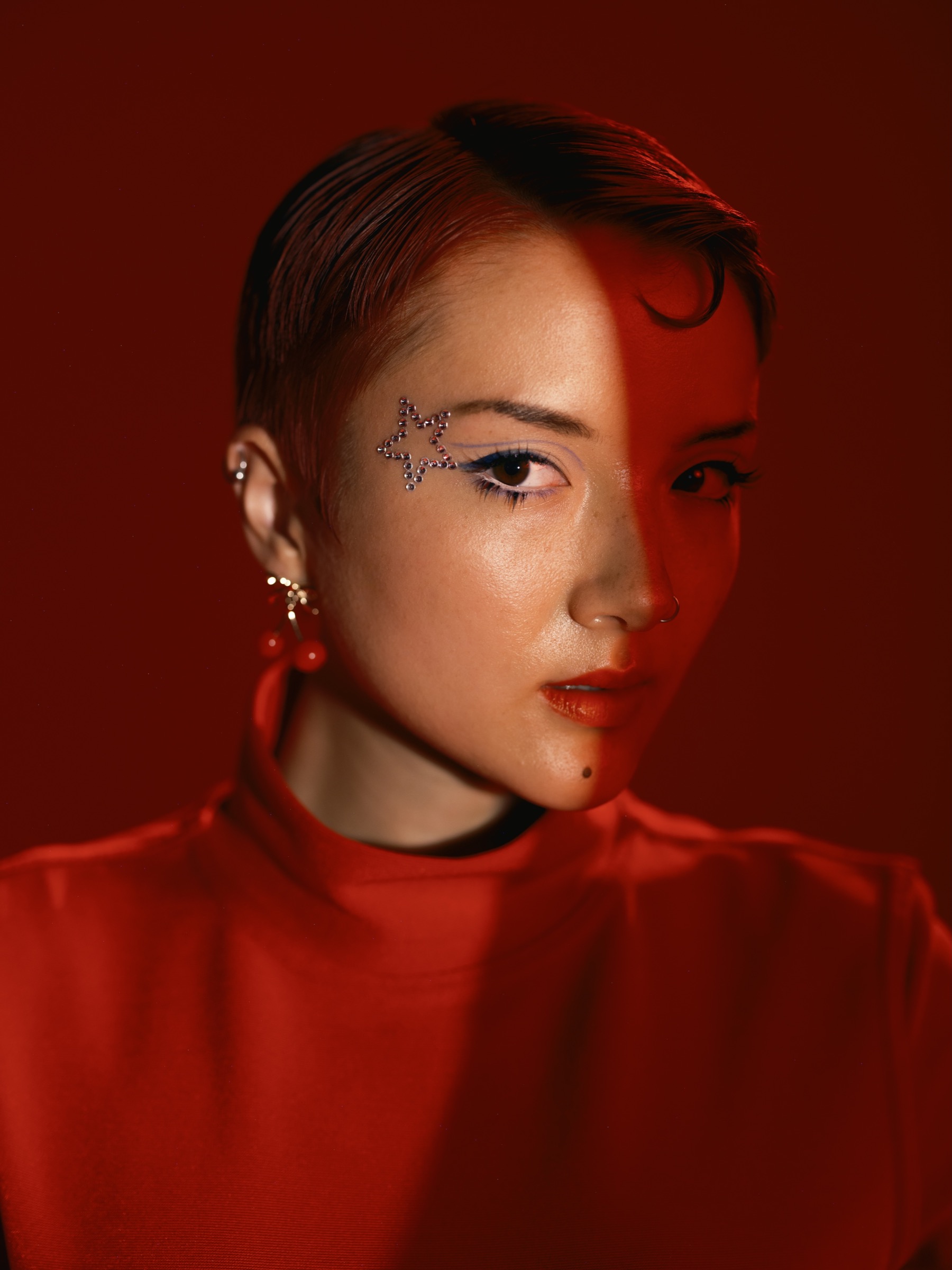 Red-lit editorial beauty portrait with star makeup