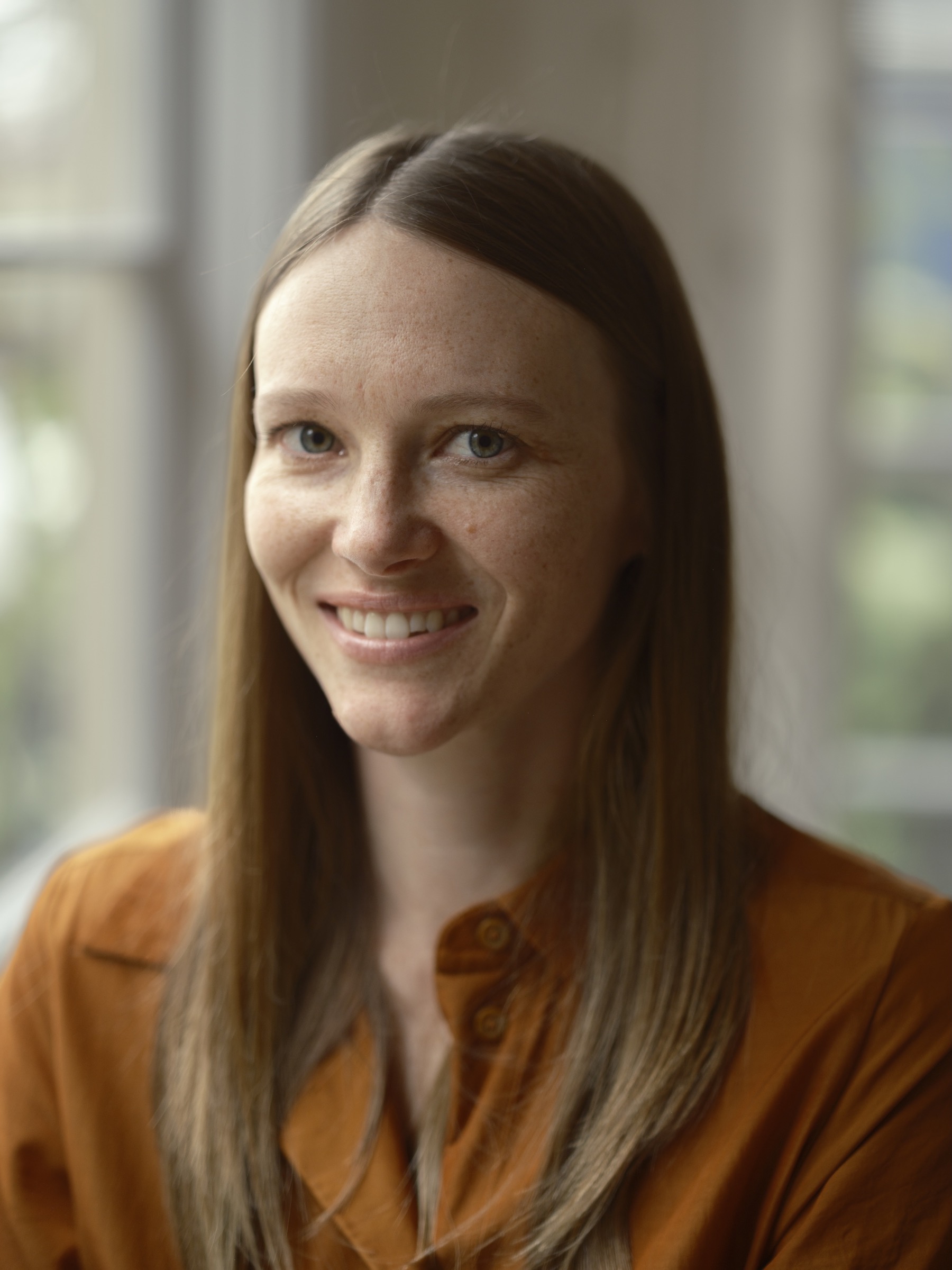 Smiling professional portrait of a woman in a rust-colored shirt