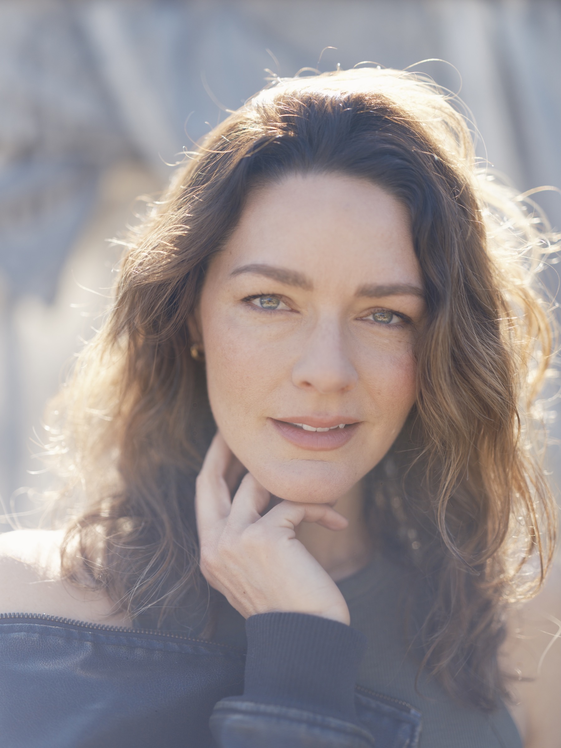 Backlit outdoor portrait of a brown-haired woman looking into the camera
